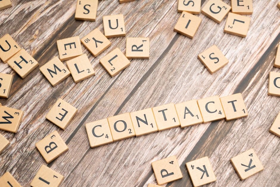 Scrabble-style letter tiles spelling 'contact' on wooden surface.