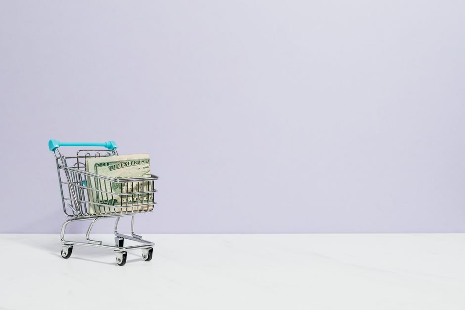 Shopping cart filled with cash on a plain background, ideal for finance and retail themes.